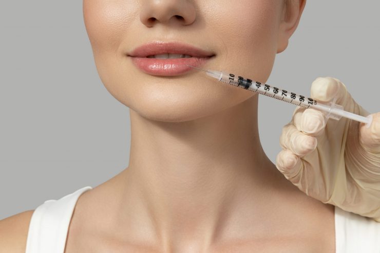 A beautiful girl makes an injection in the lips, on a gray background